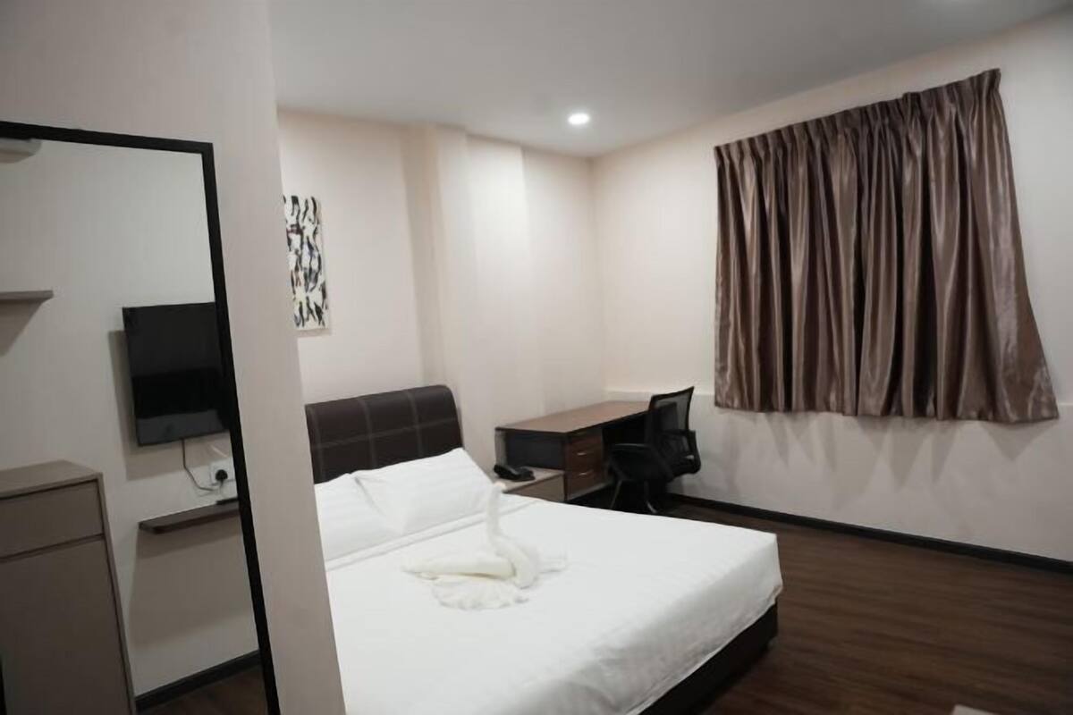 A hotel room with a bed, a desk, a chair, a TV, and a curtain.