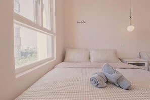 Una camera da letto con un letto, cuscini, una finestra e un punto luce a parete.