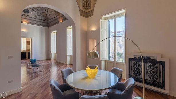 Un coin repas comprenant une table ronde en verre, six chaises et une lampe suspendue au design moderne.