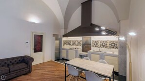 A modern kitchen with a central island, a dining area with a table and chairs, and a dark-colored sofa in a room with wooden flooring and white walls. - Il forno antico - One Bedroom Apartment, Sleeps 4 (Lecce)