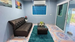 A living room with a brown sofa, a small table with a vase, a blue window, and patterned flooring. - Earnhomestay sichon (Sichon)
