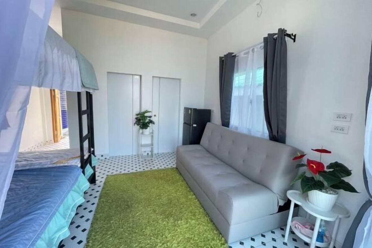 Ein kompaktes Hotelzimmer mit einem Stockbett, einer Schlafcouch, einem kleinen Tisch mit Pflanze und einer Topfpflanze auf der Couch.