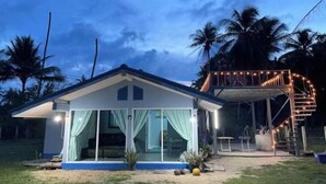 A two-story house with a covered outdoor area, large windows, and a staircase with string lights. - Earnhomestay sichon (Sichon)