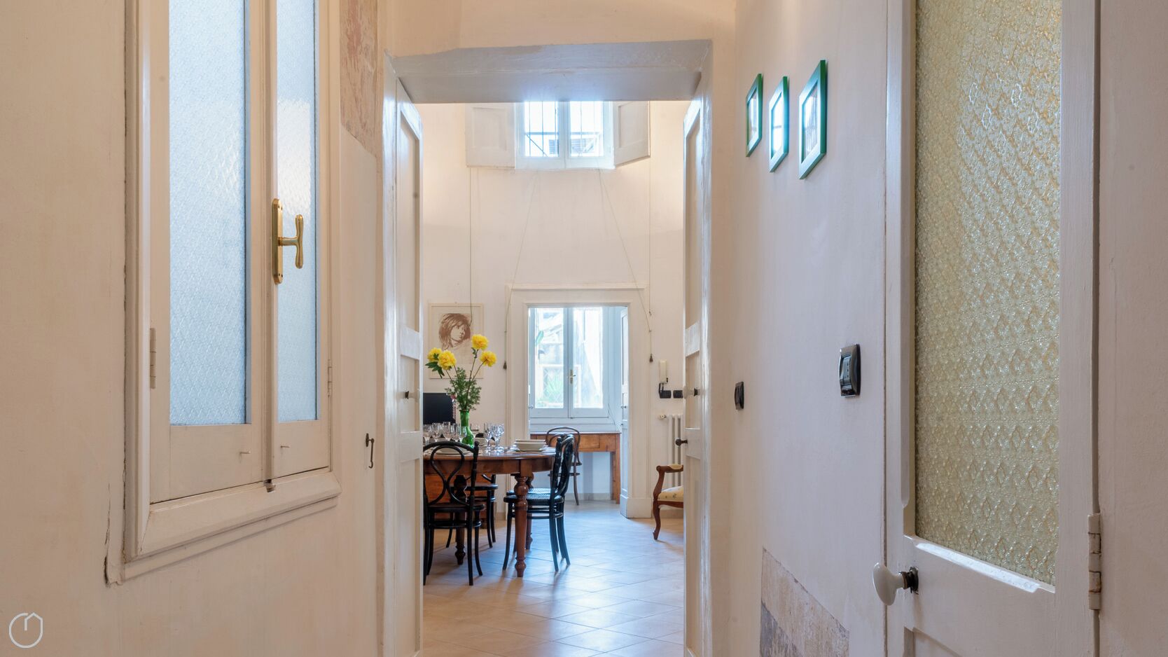 Ein Flur, der in einen Essbereich führt, mit einem für vier Personen gedecktem Tisch, einer Blumenvase und einem Fenster mit Aussicht.