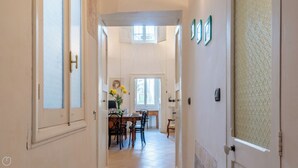 A hallway leading to a dining area with a table set for four, a vase with flowers, and a window with a view. - Casa del Barone - Three Bedroom Apartment, Sleeps 7 (Lecce)