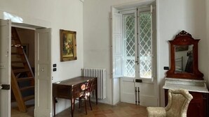 A room with a high arched ceiling, a dining table with chairs, a radiator, a large window with a lattice design, a wooden chair, and a bed with a headboard. - Casa del Barone - Three Bedroom Apartment, Sleeps 7 (Lecce)