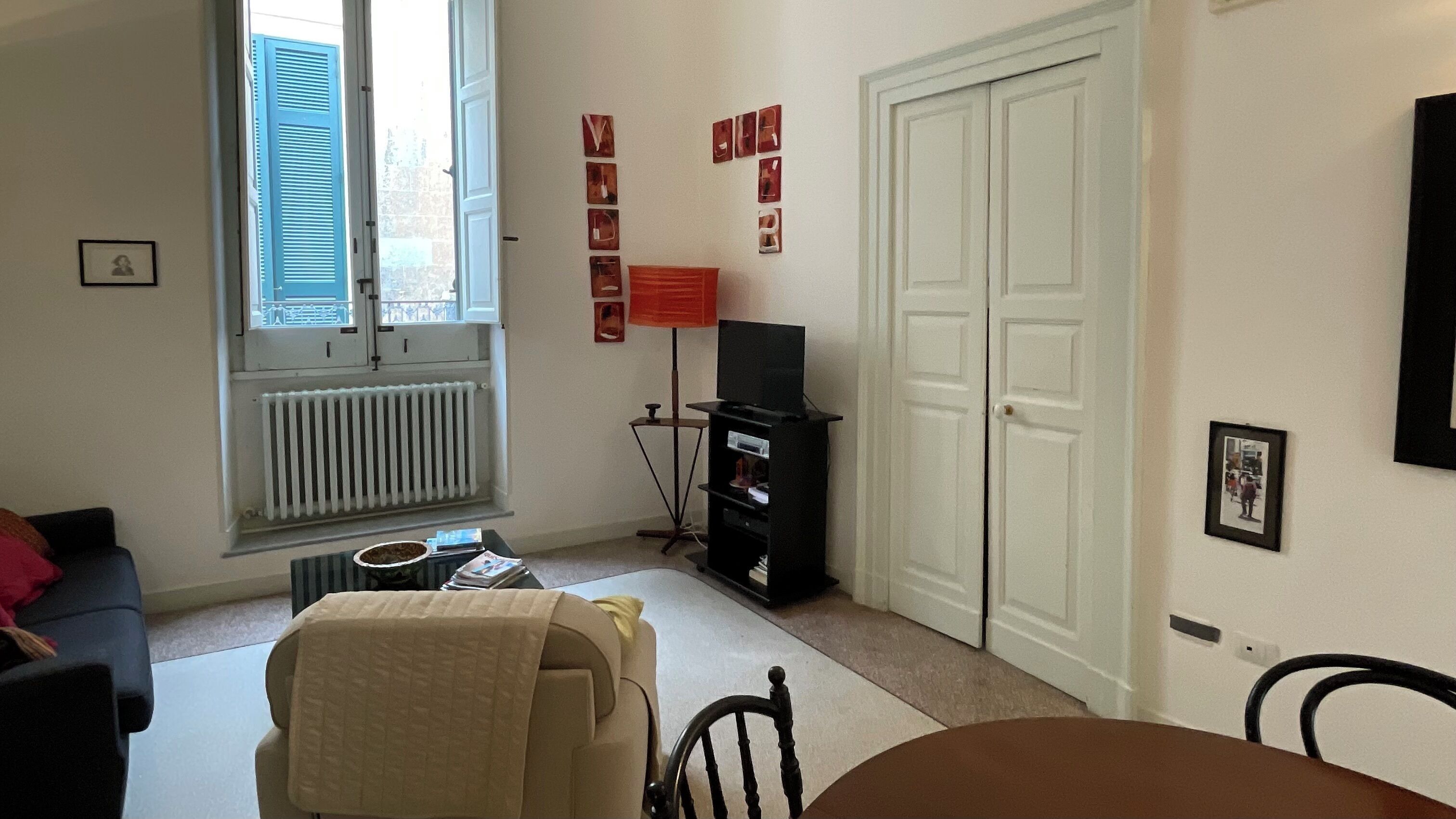 A living room with a sofa, a table, a TV on a stand, a radiator, and a door.