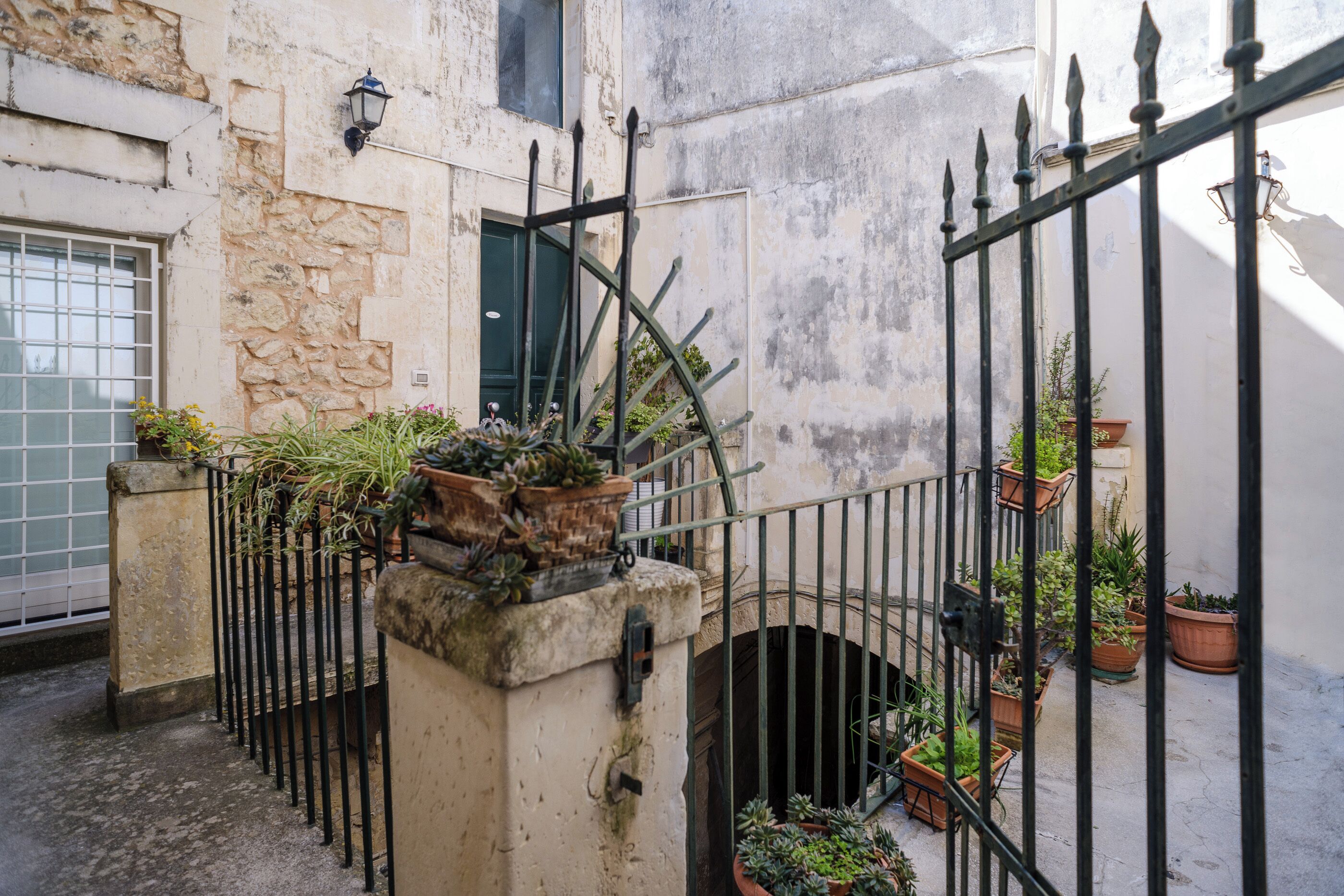 Un cortile stretto con un muro in pietra, un cancello in metallo e piante in vaso.