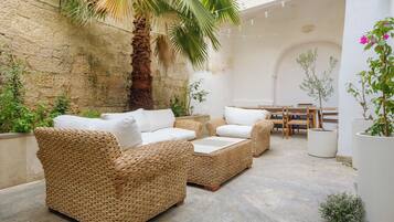 Ein Rattansitzgruppe mit Kissen, eine Palme und ein Esstisch mit Stühlen in einem Innenhof.