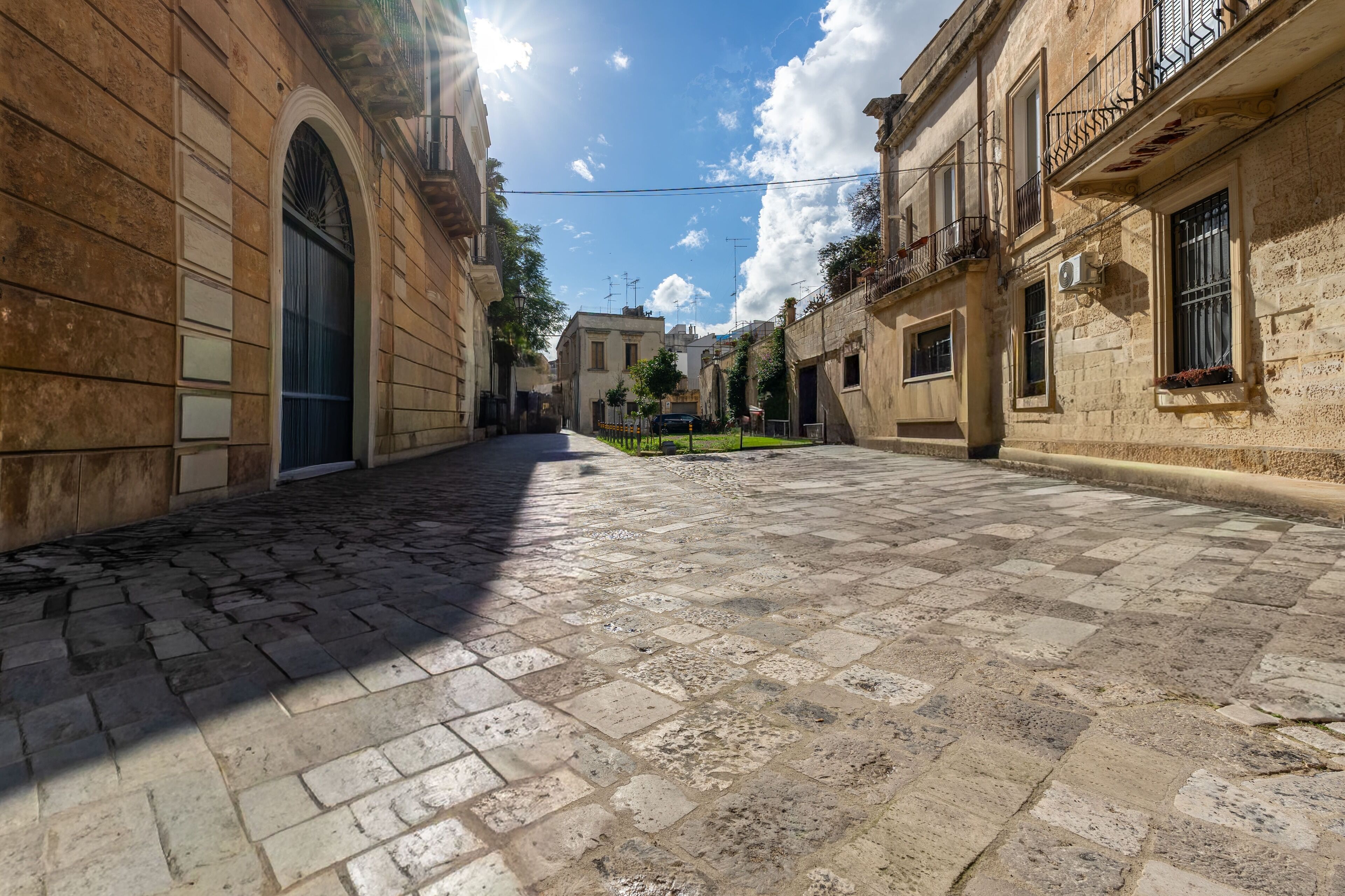Una strada acciottolata con edifici storici, un'ampia porta ad arco e cielo sereno.