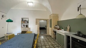 A compact kitchen with a tiled floor, a dining area with a table and chairs, a bookshelf, and a small window. - Giurdana 0dB - One Bedroom House, Sleeps 3 (San Cesario di Lecce)
