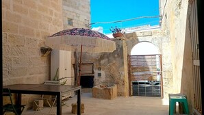 A courtyard with a table and chairs, a potted plant, and a patterned umbrella. - Giurdana 0dB - One Bedroom House, Sleeps 3 (San Cesario di Lecce)