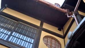 A traditional building with a wooden beam structure, a window with a grid pattern, and a small circular window with a lattice design. - Kyo No Ondokoro Gokomachi Ebisugawa #3 (Kyoto)