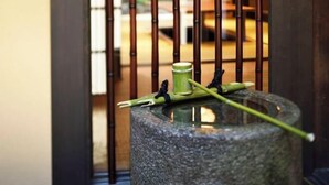 A stone water feature with a bamboo stick and a green leaf on top, surrounded by a bamboo fence. - Kyo No Ondokoro Gokomachi Ebisugawa #3 (Kyoto)