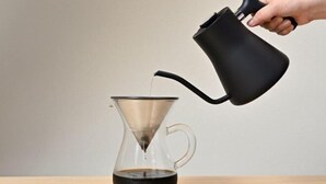 A hand pouring coffee from a black pitcher into a clear glass carafe with a metal filter. - Kyo No Ondokoro Gokomachi Ebisugawa #3 (Kyoto)