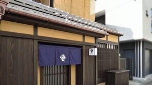 A traditional Japanese building with a wooden gate, a blue awning with a logo, and a small sign on the wall. - Kyo No Ondokoro Gokomachi Ebisugawa #3 (Kyoto)