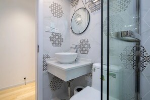 Een moderne badkamer met een witte wastafel, een ronde spiegel en een douchecabine van glas.