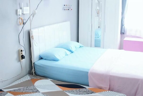 A bedroom with a bed, a bedside table, a mirror, and a wall-mounted power outlet.