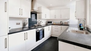 A modern kitchen with white cabinets, a black countertop, and stainless steel appliances. - Big Family Home! FREE Parking, Fast WiFi, Garden (Kingston upon Thames)