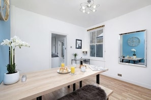 A modern dining area with a wooden table, chairs, a bench, a potted plant, and a wall clock. - Big Family Home! FREE Parking, Fast WiFi, Garden (Kingston upon Thames)