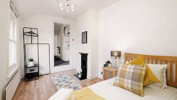 A bedroom with a bed, a bedside table, a lamp, a hanging plant, and a view of a hallway.