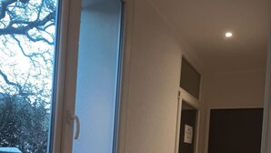 A narrow hallway with a large window on the left, a door at the end, and a light fixture on the ceiling. - Studio 2 in quiet renovated 2023. Garage (Saint-Pierre-des-Corps)