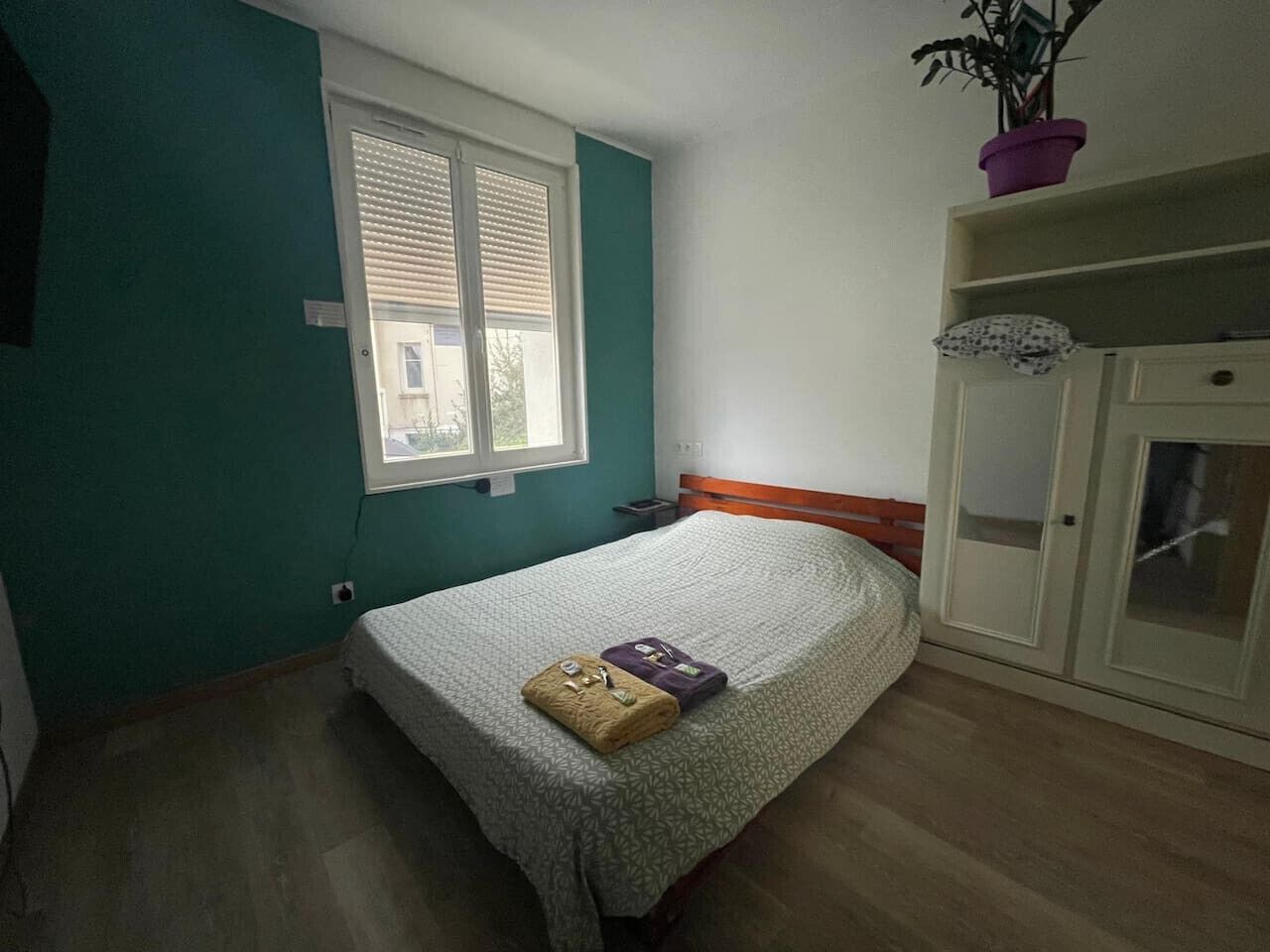 Una camera da letto con un letto, una finestra, un armadio e una pianta in vaso.
