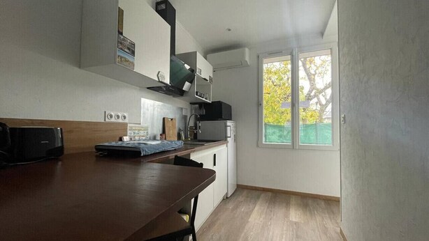A modern kitchen with a wooden table, white cabinets, and a large window with a view of trees. - Studio 2 in quiet renovated 2023. Garage (Saint-Pierre-des-Corps)