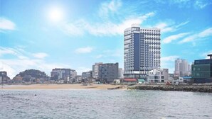A coastal cityscape with a prominent high-rise building, a sandy beach, and a calm sea. - Lighthouse Beach 1504 (Sokcho-si)