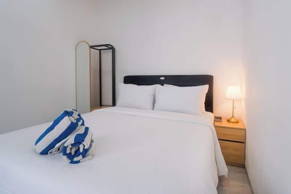 Et hotelværelse med en seng, et natbord med en lampe og et foldet håndklæde.