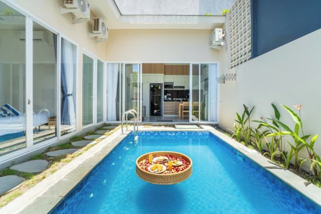 A modern pool with a floating basket of food, surrounded by glass doors and a well-maintained garden.