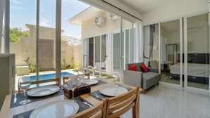 Una habitación de hotel moderna con zona de comedor, piscina y balcón con sofá.