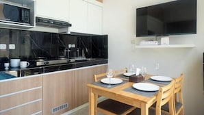 Una cocina moderna con encimera negra, armarios blancos y microondas integrado. Se observa una mesa de comedor con sillas y un televisor de pantalla plana montado en la pared.