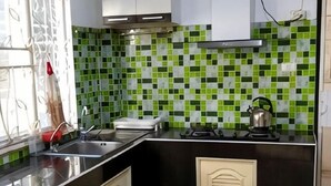 A kitchen with a black countertop, a stainless steel sink, a kettle, and a green-tiled backsplash. - Centraltesco/ NightSafari/4Bedroom Villa (Chiang Mai)