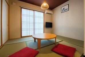 A tatami mat room with a sliding shoji door, a round table, and two red cushions. - Sakuragawa-an Higashiyama (Kyoto)