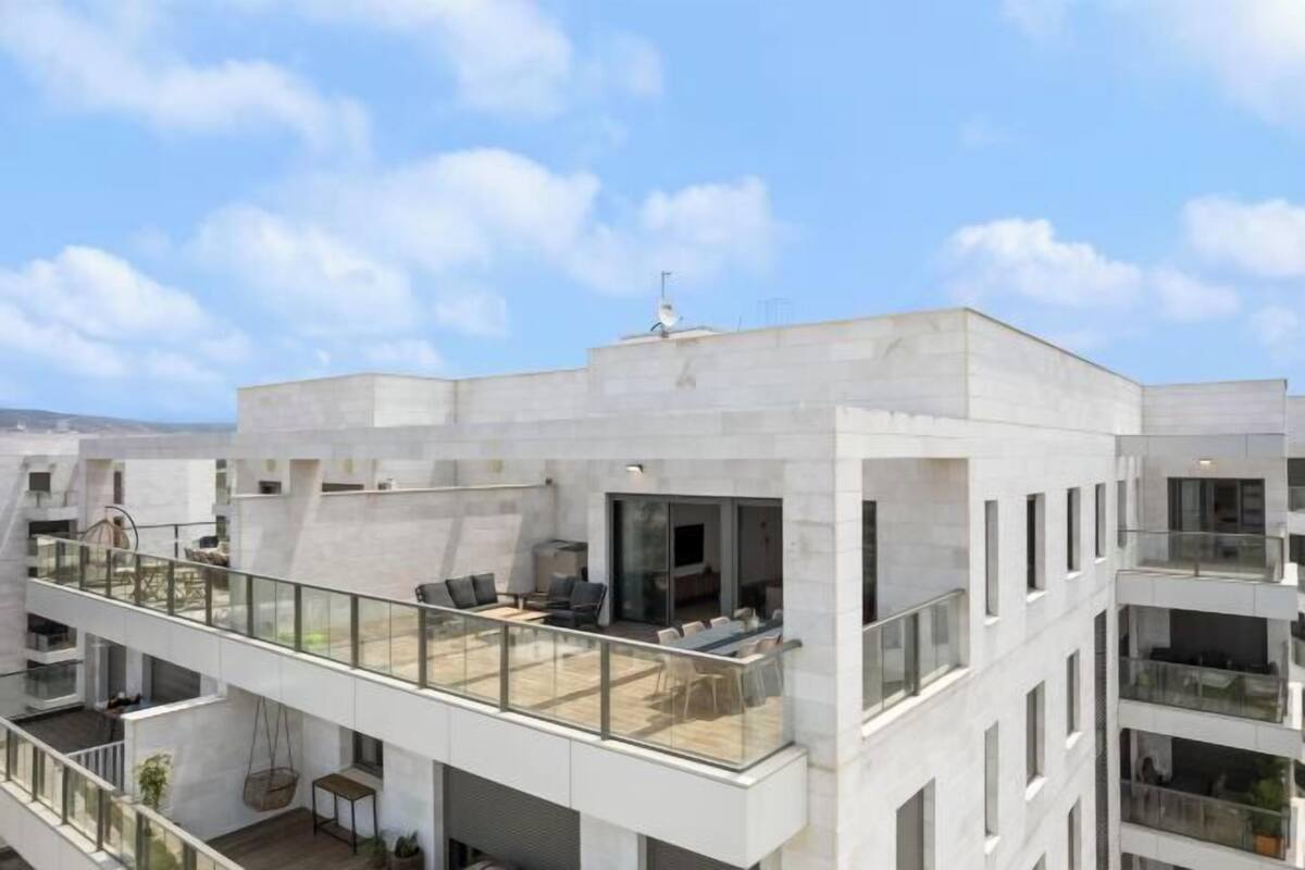 Un immeuble résidentiel moderne à plusieurs étages, doté d’un toit plat, de grandes fenêtres et d’un balcon avec un espace salon extérieur.