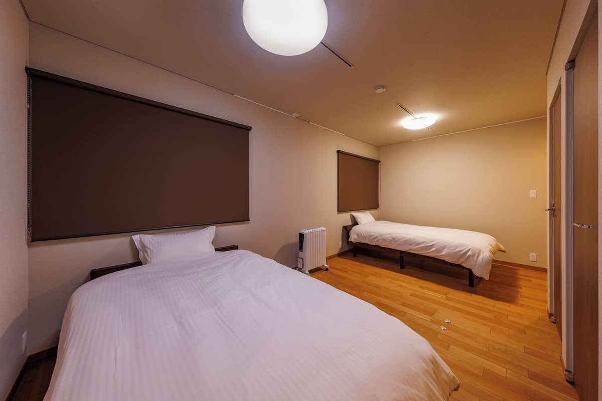 A hotel room with two beds, a large window, a radiator, and a ceiling light.