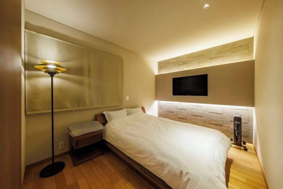 A bedroom with a bed, a bench, a standing lamp, a TV, and a workout machine.