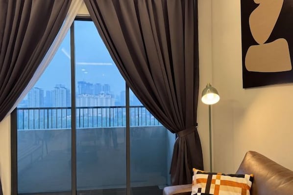A room with a large window, a floor lamp, and a couch with a patterned cushion.