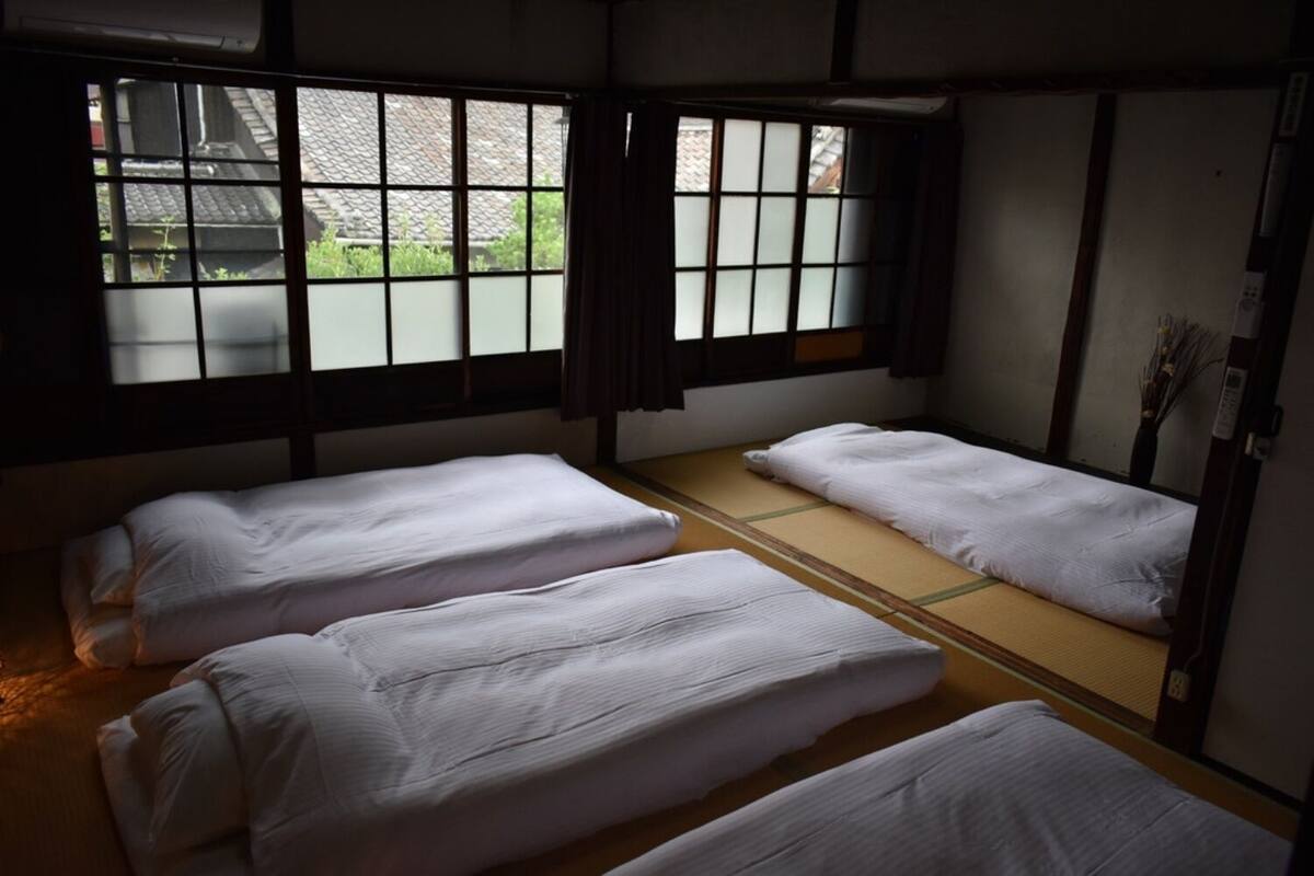 Habitació japonesa tradicional amb paviment de tatami, un panell shoji i tres estris de tatami amb roba de llit blanca.