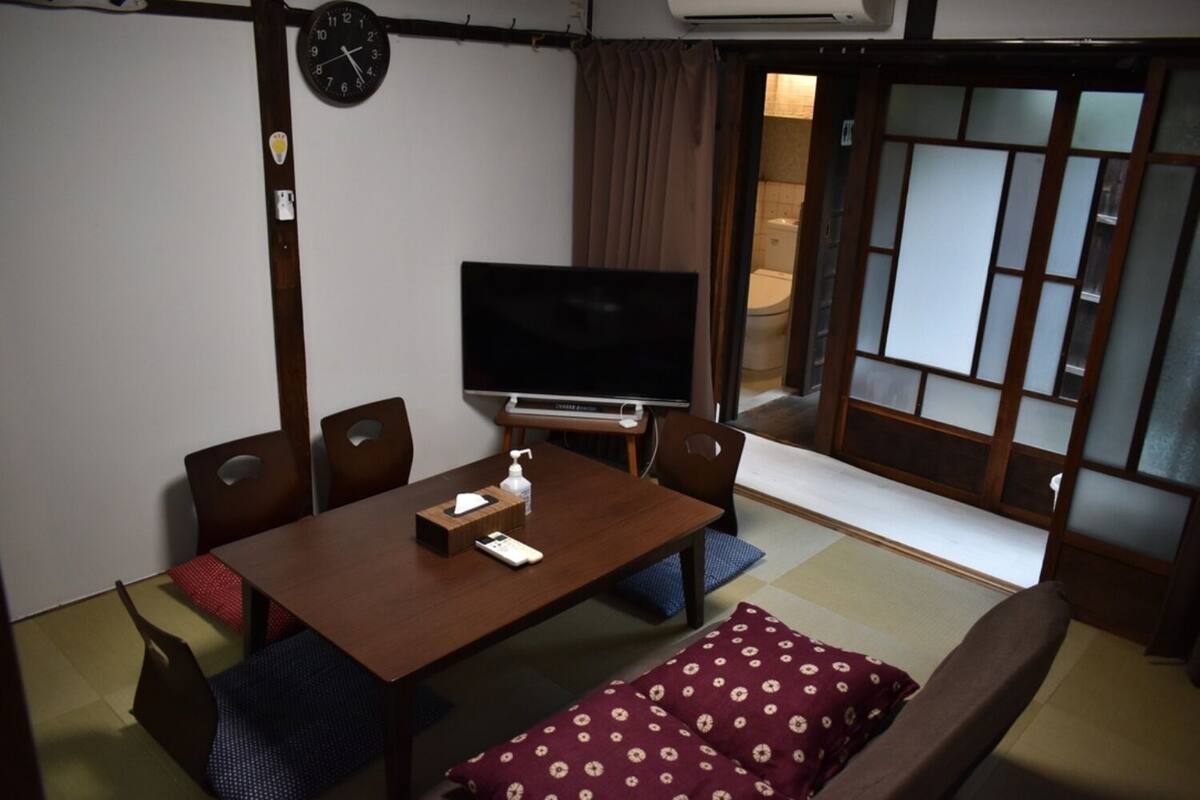 Habitació japonesa tradicional amb paviment de tatami, una taula baixa amb televisió i una porta corredissa que dona a un bany.
