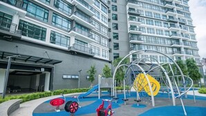 A playground with swings and a slide, a building with multiple floors and balconies, and a covered entrance. - Molek Little Joy Studio 4pax Bathtub with Balcony (Plentong)