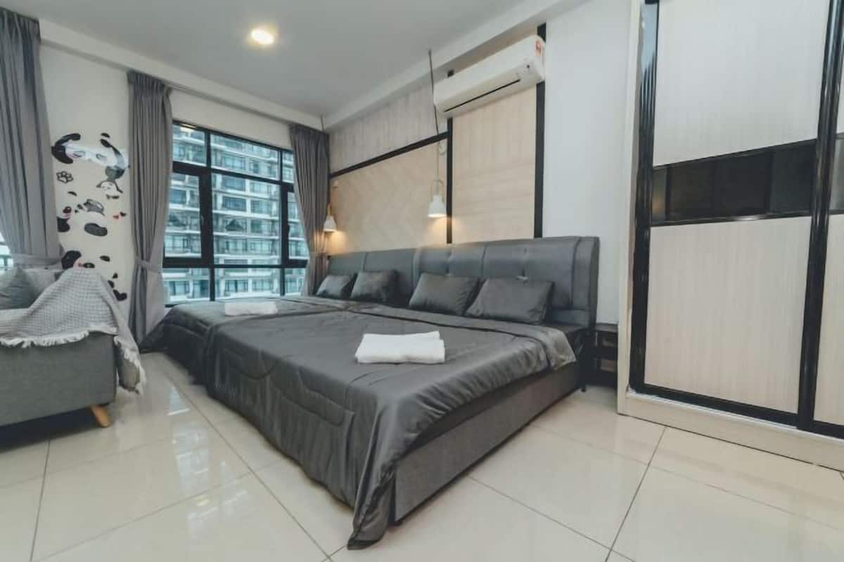 A modern bedroom with a large bed, a sofa, a wardrobe, and a window with a city view.