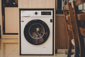 A front-loading washing machine in a modern kitchen with wooden cabinets and a tiled floor. - Molek Little Joy Studio 4pax Bathtub with Balcony (Plentong)