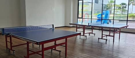 Una habitación con dos mesas de ping pong, ventanas amplias y suelo de madera.