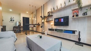 A modern living room with a sofa, a coffee table, a TV mounted on the wall, and a dining area with chairs and a table. - Molek Little Joy Studio 4pax Bathtub with Balcony (Plentong)