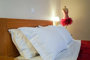A bed with white bedding, a wooden headboard, and a mannequin with a red feathered dress. - Villa Mykines (Mykines)