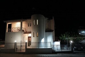A white building with a balcony, a staircase, and a gated entrance at night. - Villa Mykines (Mykines)