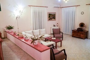 A living room with a sofa, a coffee table, and a dining area with a long table. - Villa Mykines (Mykines)