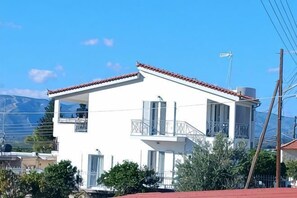 A two-story white building with a red-tiled roof, balconies, and a view of mountains. - Villa Mykines (Mykines)